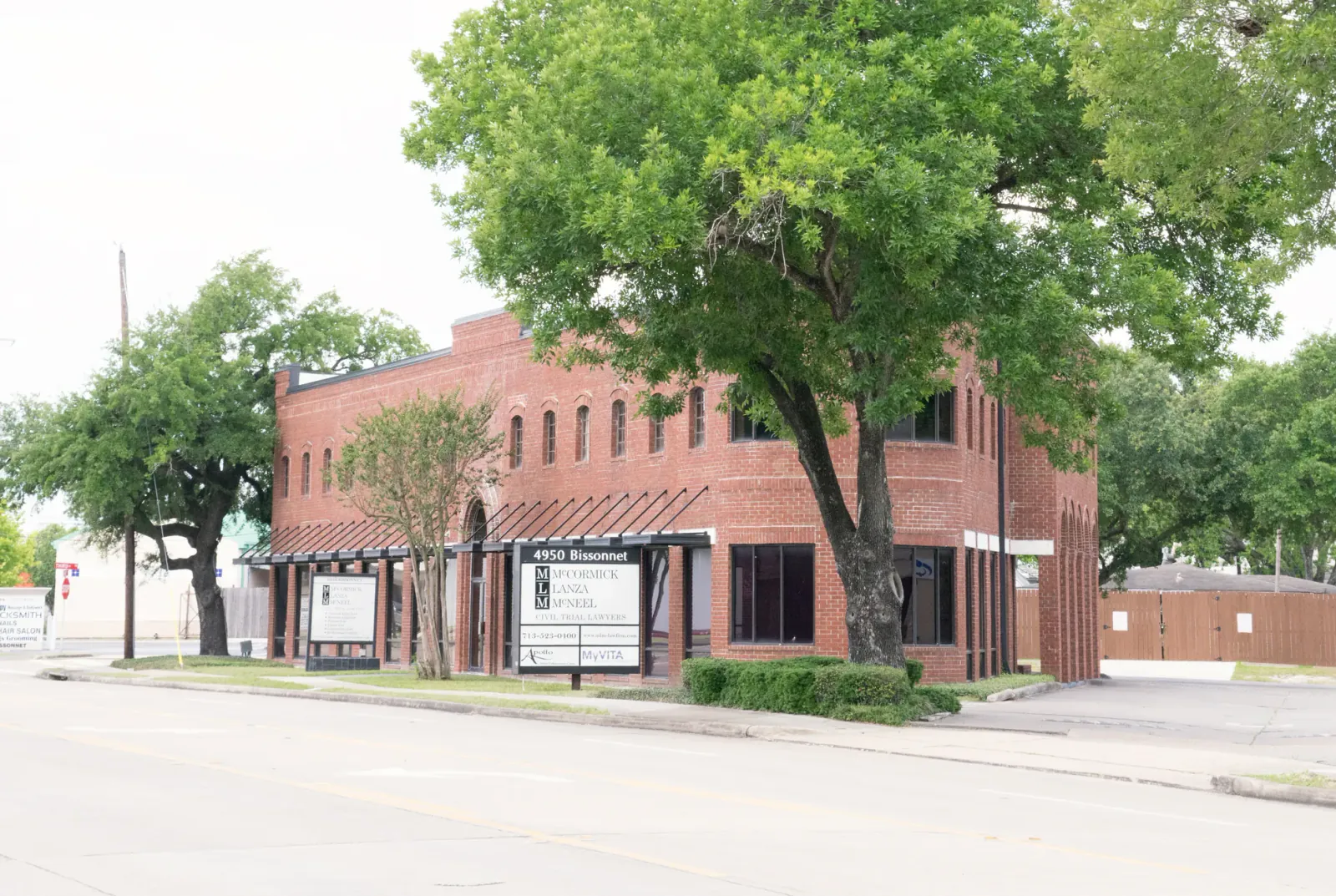 Two-story red-brick commercial building on a tree-lined street