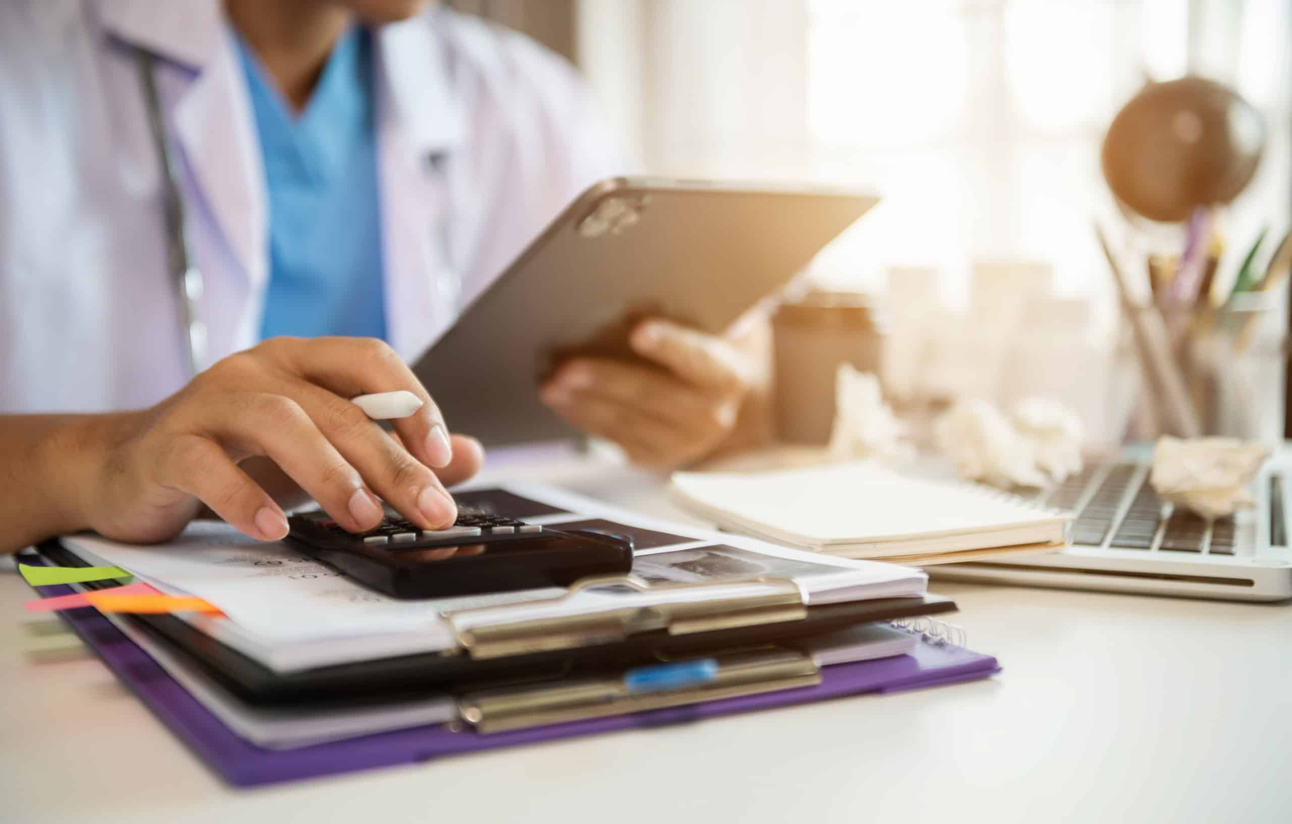 A doctor is utilizing a tablet at his desk to access local healthcare insurance benefits.