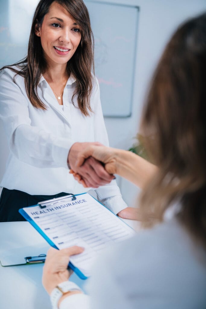 A woman shaking hands with another woman in an office conducting a business agreement.
