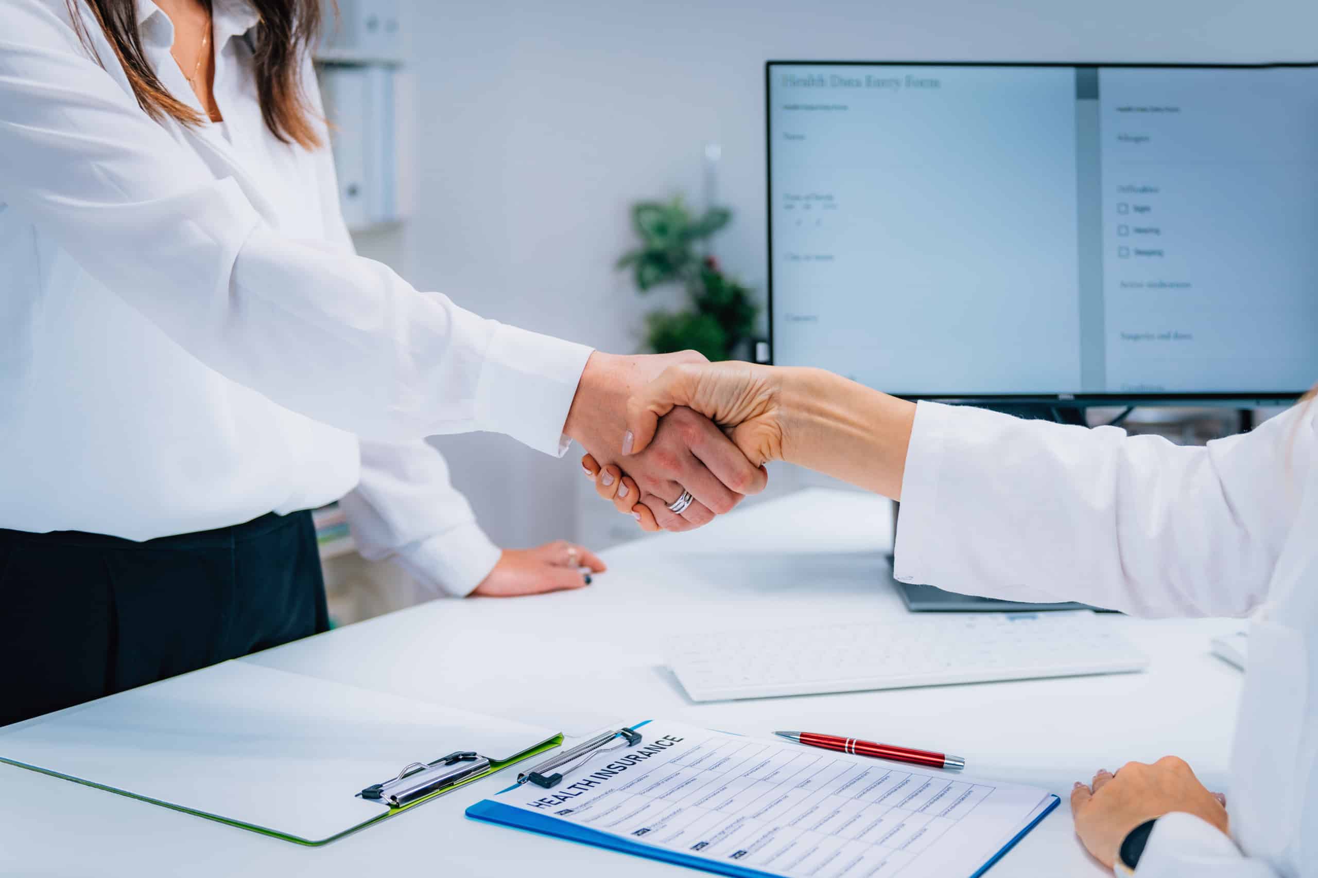 Two health insurance professionals shaking hands in front of a desk.