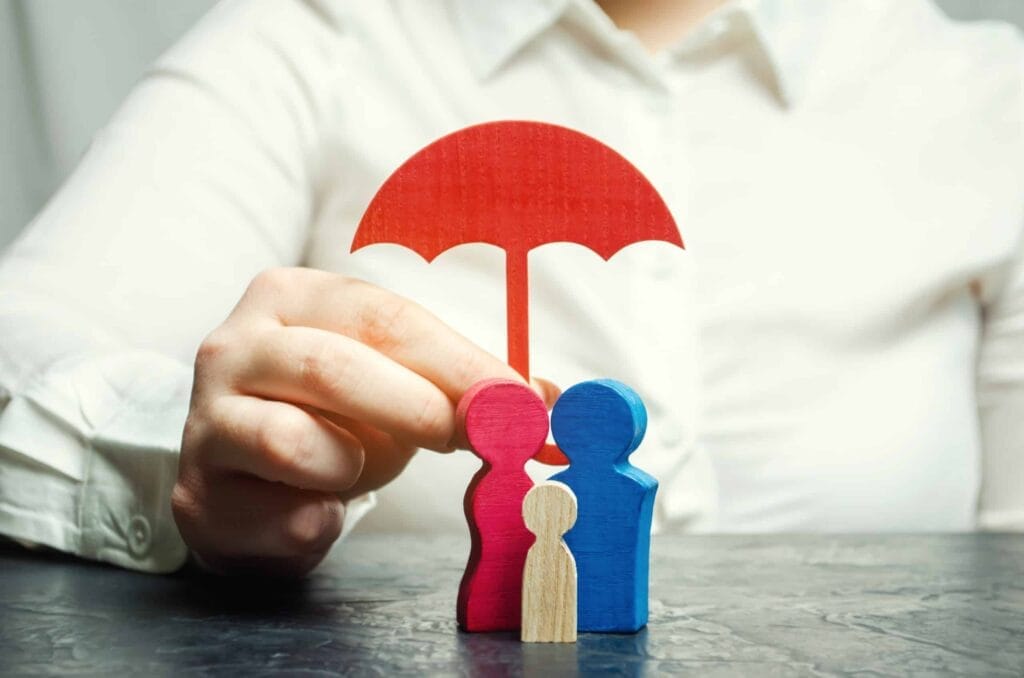 A woman demonstrates reference based pricing by covering a wooden figure of a family with her red and blue umbrella.